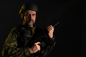Fototapeta premium Soldier in military uniform and helmet with weapon looking at camera on black background.