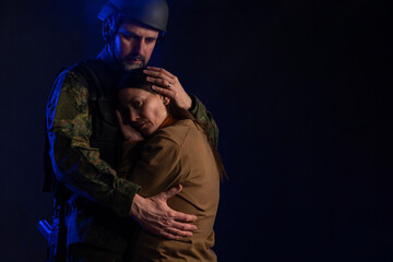 Sad woman hugging her military husband and saying-goodby to him before going to army on black backgound.