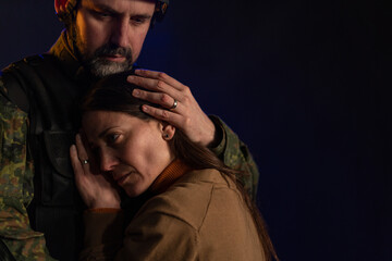 Sad woman hugging her military husband and saying-goodby to him before going to army on black backgound.