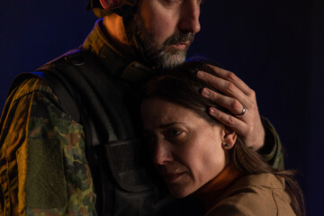 Sad woman hugging her military husband and saying-goodby to him before going to army on black...