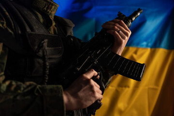 Fototapeta premium Close-up of soldier in military uniform holding weapon with Ukraine flag in background.