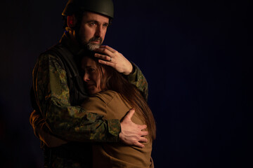 Fototapeta premium Sad woman hugging her military husband and saying-goodby to him before going to army on black backgound.