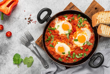 Shakshuka in a frying pan on a gray rustic background. Jewish scrambled eggs. Poached eggs in a spicy tomato pepper sauce. Top view, flat lay.