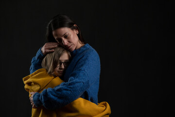 Sad mother hugging her daughter, both wearing Ukrainian national colors on black background.