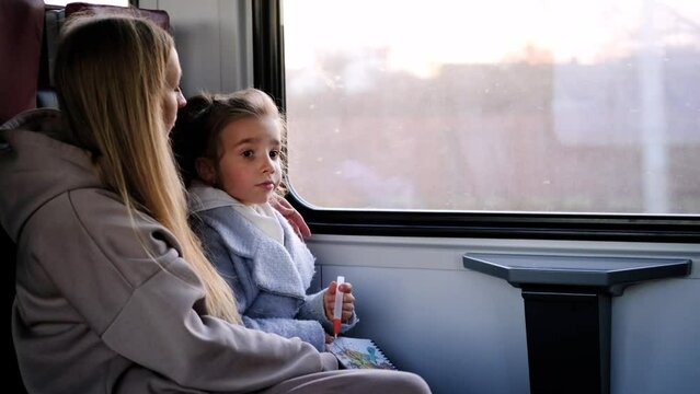 Mom and daughter are on the train and look out the window. 