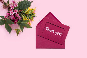 Beautiful bouquet of flowers of delicate weigela on pink background. Envelope and letter with the inscription Thank you! Minimal concept backdrop.