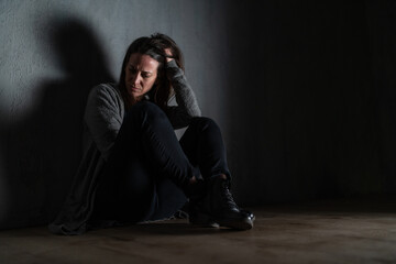 Sad mid-adult woman, alone in darkness, sitting and thinking.