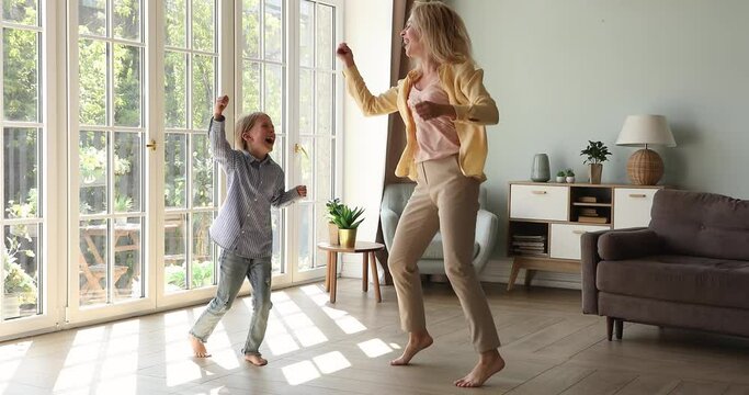 Cheerful happy young woman her little 6s cute daughter listen favourite music having fun dancing barefoot on warm floor in modern spacious living room. Family active weekend leisure and hobby concept