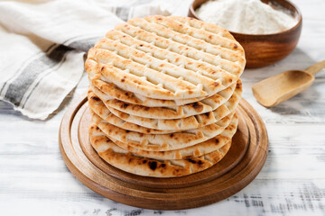 Fresh baked greek pita bread on white wooden background.