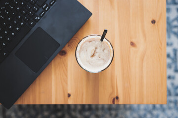 soy latte in a clear mug next to laptop on dining table, remote working or coffee break at the office