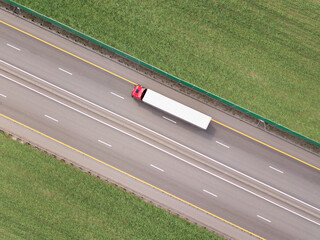 Dump trucks carrying goods on the highway. Red truck driving on asphalt road along the green fields. seen from the air. Aerial view landscape. drone photography. cargo delivery