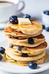 Stack of blueberry pancakes with maple syrup and butter on white plate for breakfast.