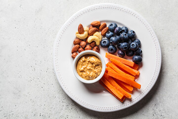 Vegan snacks plate - carrots, nuts, berries and peanut butter, top view.