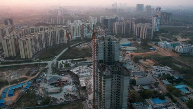 orbiting hyper lapse shot around under construction sky scraper tower with crane on top and trucks moving on the base showing the rapid development in Indian cities like Delhi, Gurgaon, Noida and more
