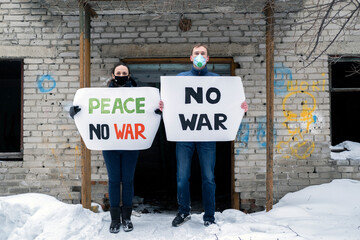Man and Woman Holding Banners Against War Conflict by Abandoned Brick Building, Protesting Manifestation 
