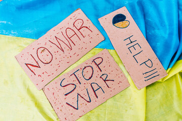 3 cardboard signs that say: 'Help' next to a blue and yellow heart, 'no war' and 'Stop war' against the background of the colors of the Ukrainian flag. Ukraine, Russia, inplane war concept.