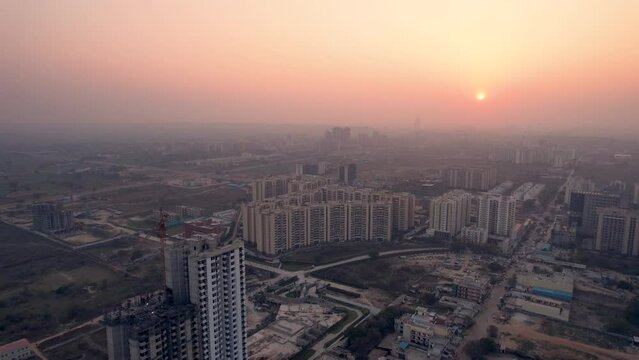 slow aerial shot going towards sunset showing under construction skyscraper with crane and smaller apartment buildings showing the rapidly increasing real estate infrastructure with homes, offices in