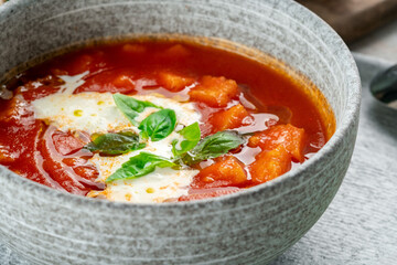 Italian vegetable soup with tomatoes, basil, cheese and vegetables in a gray bowl. Tomato cream soup close up