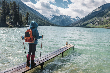 Hiker girl traveler stands on a wooden pier for fishing boats on a scenic mountain lake