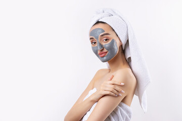 A woman with a gray clay cosmetic mask in a white towel on her head on a white background.