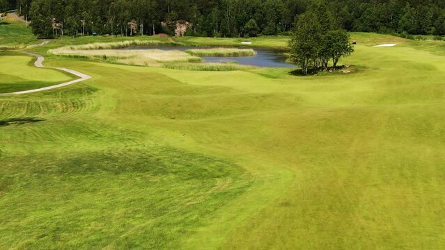 Back view of golfer and caddy walking on golf course towards water obstacle. Aerial forward