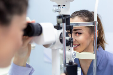 Female doctor ophthalmologist is checking the eye vision of attractive young woman in modern clinic. Doctor and patient in ophthalmology clinic. - obrazy, fototapety, plakaty