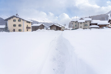 Footprints on pathway in snowdrifts leading towards homes in mountain village. The way forward or...