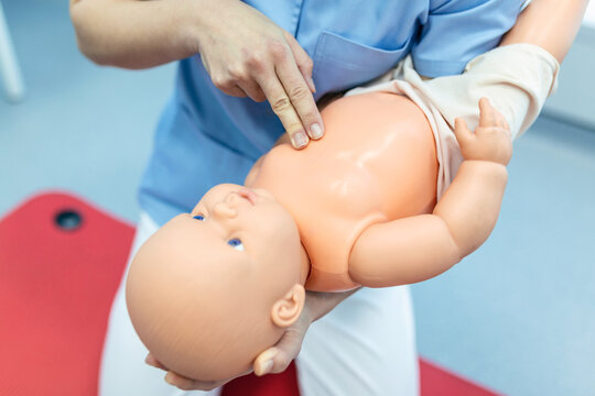 Woman performing CPR on baby training doll with one hand compression. First Aid Training - Cardiopulmonary resuscitation. First aid course on cpr dummy.