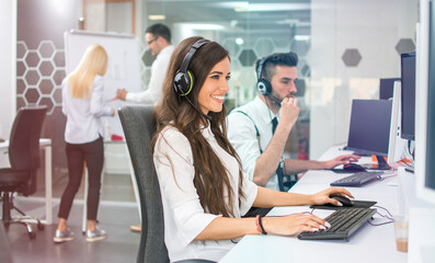 Young positive woman customer support phone operator in microphone headset working on computer in the office