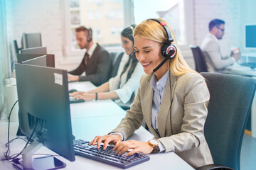 Young blonde haired woman in headset, sitting in office, working as operator of call center or...