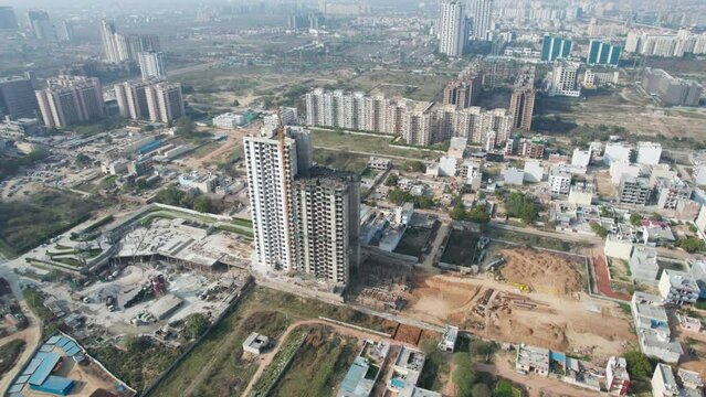aerial rail shot showing under construction multi story building with crane on top and empty barren grounds all around filled with equipment in Noida, Gurgaon India