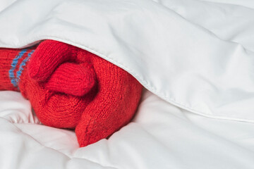 Womens hands in red mittens on white blanket. The warmth of home comfort.