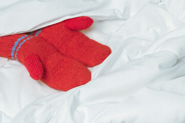 Womens hands in red mittens on white blanket. The warmth of home comfort.