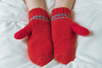 Womens hands in red mittens on white blanket. The warmth of home comfort.