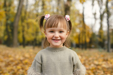 Cute little girl is laughing in the autumn forest among the yellow leaves