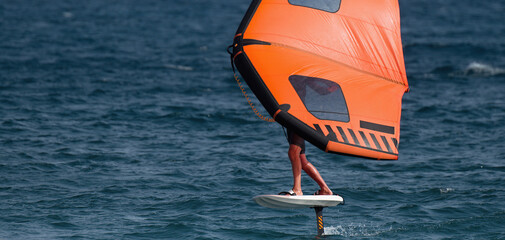 A man is wing foiling using handheld inflatable wings and hydrofoil surfboards in a blue ocean, rider on a wind wing board, surf the waves
