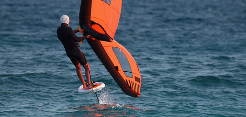 A man is wing foiling using handheld inflatable wings and hydrofoil surfboards in a blue ocean,...