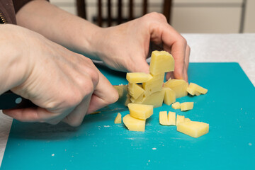 A woman cuts a boiled potato with a knife for a festive salad on a green board, only her hands are visible close-up