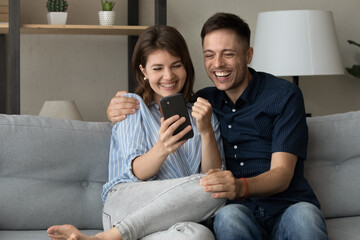 Cheerful emotional young 30s married couple making yes gesture looking at smartphone screen, celebrating online lottery auction win or reading email with amazing news, internet success concept.