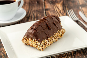 Dessert Cake from Malaga on wooden table. Cake with banana inside, covered with chocolate sauce and hazelnuts.