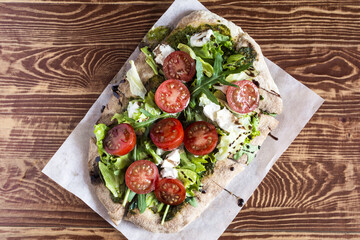 Pizza with cheese, tomatoes, cabbage and arugula on a wooden stand on a natural background.