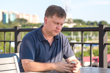 adult handsome blond man is sitting in a summer cafe at a table with view of the city.