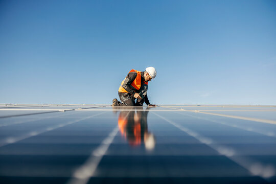 Worker kneeling and sets solar panel.