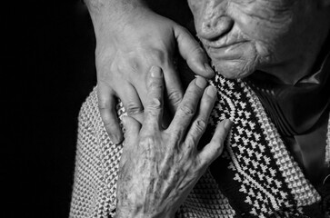 Obraz na płótnie Canvas Hands of an elderly woman against black background. black and white photo.
