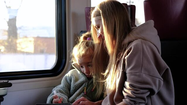 Mom helps her daughter draw a picture while they are on the train