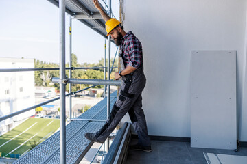 A construction site worker standing on scaffolding and taking a break from hard work.