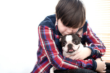 Boy lovingly hugging his happy friend boston terrier dog with a smile on his face at home. Pet care.