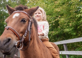 little girl riding pony without saddle on meadow in summer sunny afternoon