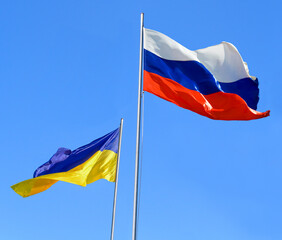Flags of Russia and Ukraine are flying in the wind against the blue sky