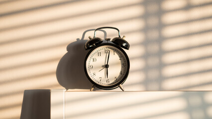 beautiful black retro alarm clock on bed head board with white wall and sunset with shade and...